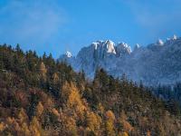 Erster Schnee am Kampenwand Gipfel mit Kreuz, darunter Herbstwald